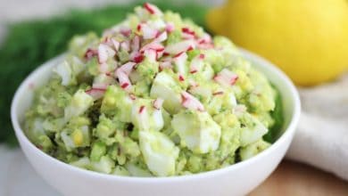 avocado egg salad in a white bowl topped with diced radishes and celery