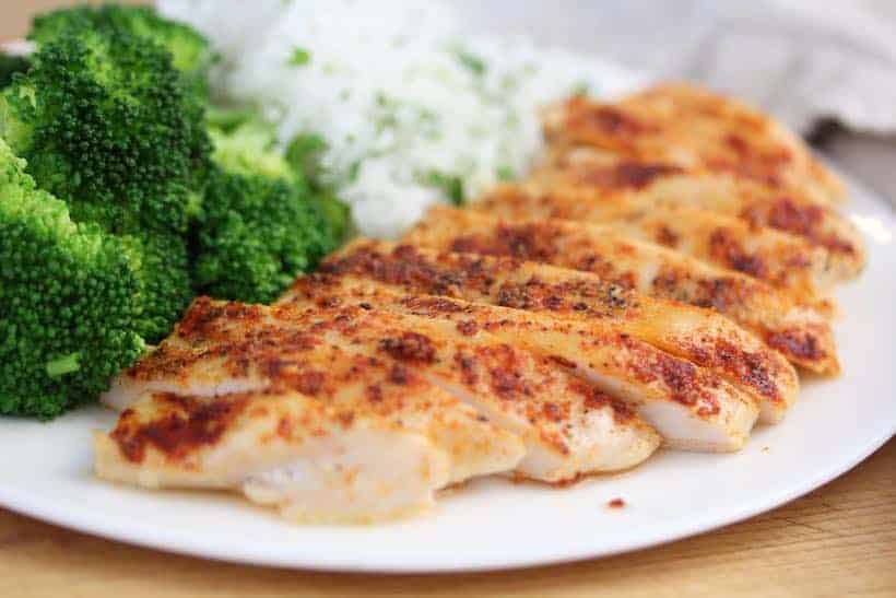baked chicken breast on a white plate with jasmine rice and steamed broccoli