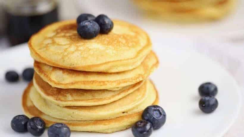fluffy coconut flour pancakes on a white plate topped with juicy blueberries