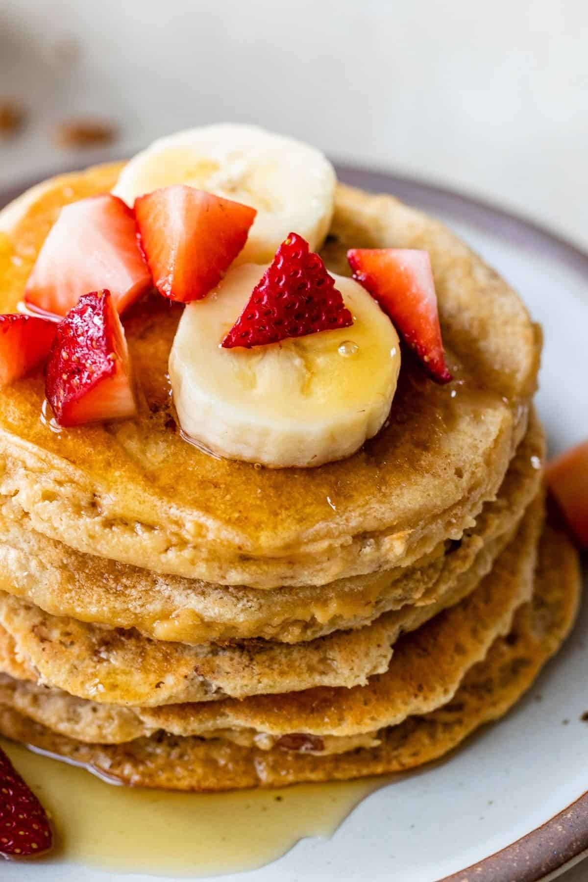 A stack of pancakes topped with syrup, berries and banana.