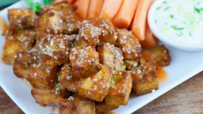 crispy baked buffalo tofu bites on a white plate with carrots and celery