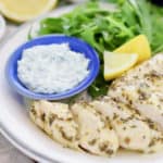 lemon garlic chicken on white plate with arugula salad, fresh lemon and dill sauce