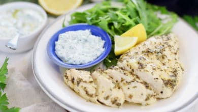 lemon garlic chicken on white plate with arugula salad, fresh lemon and dill sauce