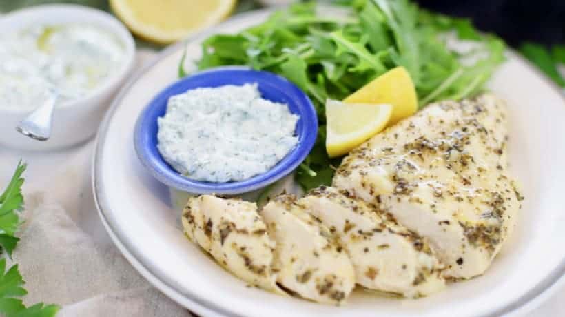 lemon garlic chicken on white plate with arugula salad, fresh lemon and dill sauce