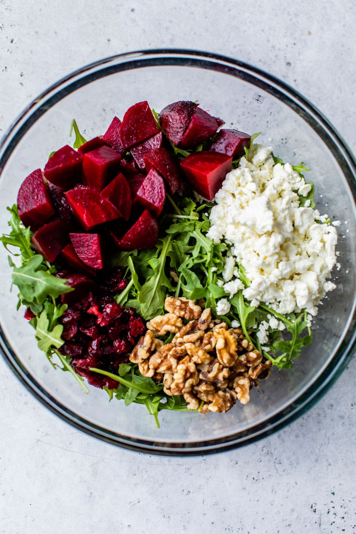 Steamed beets, arugula, goat cheese and walnuts added to a large bowl.