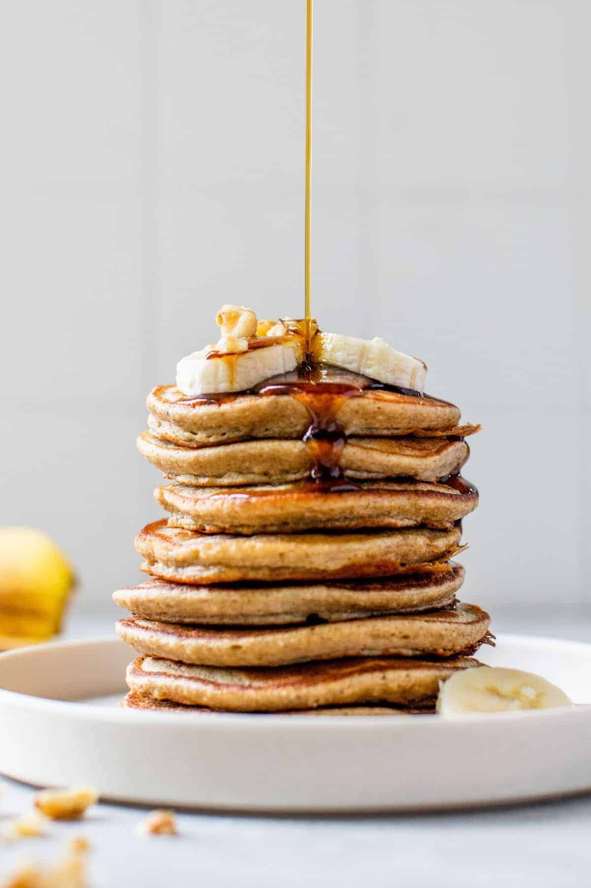 drizzling maple syrup over a stack of banana oatmeal pancakes