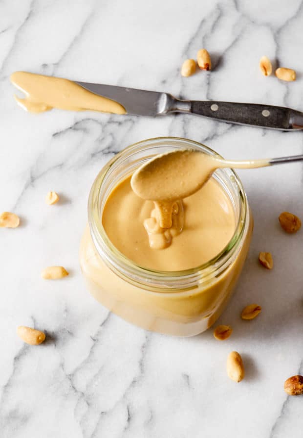 An opened jar of peanut butter with a small spoon Stock Photo