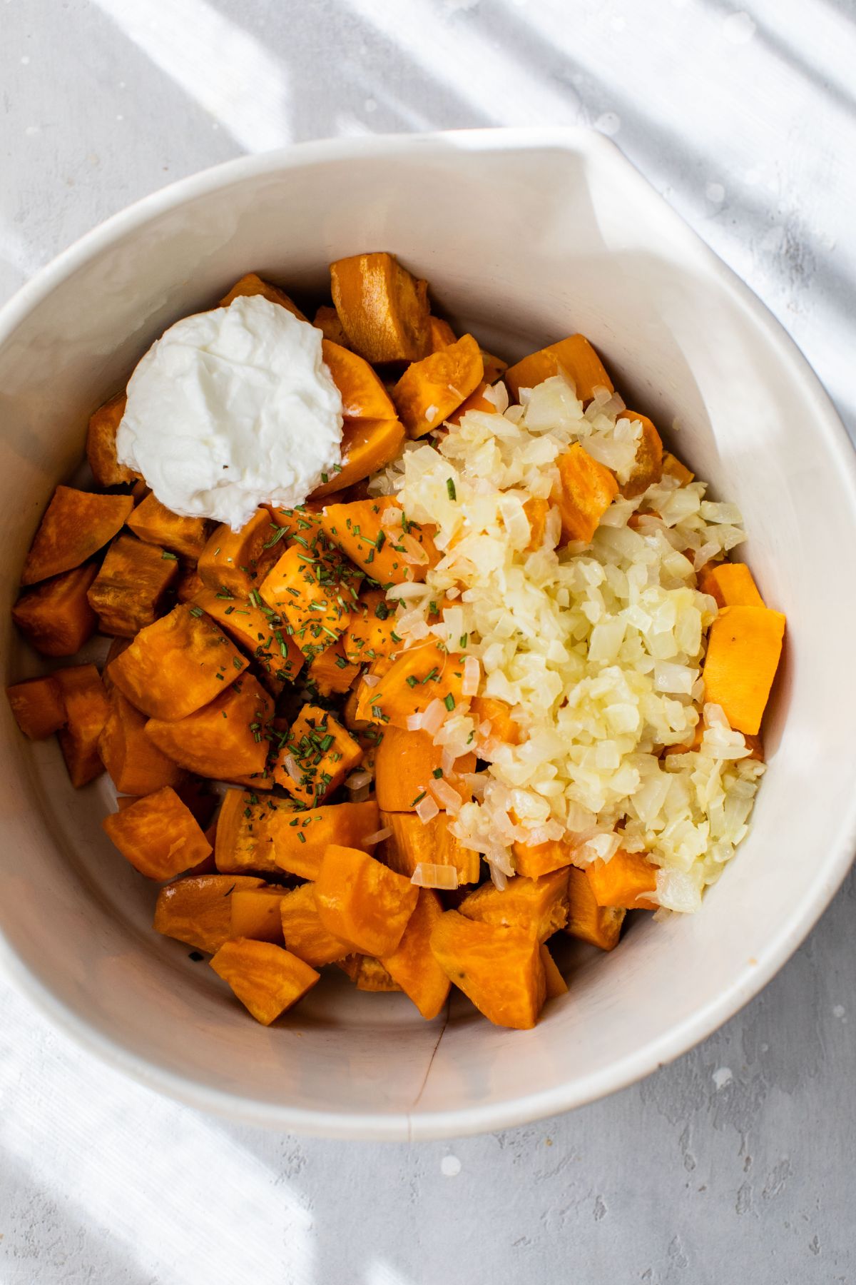 Cubed sweet potato, onion, greek yogurt and seasoning in a bowl.