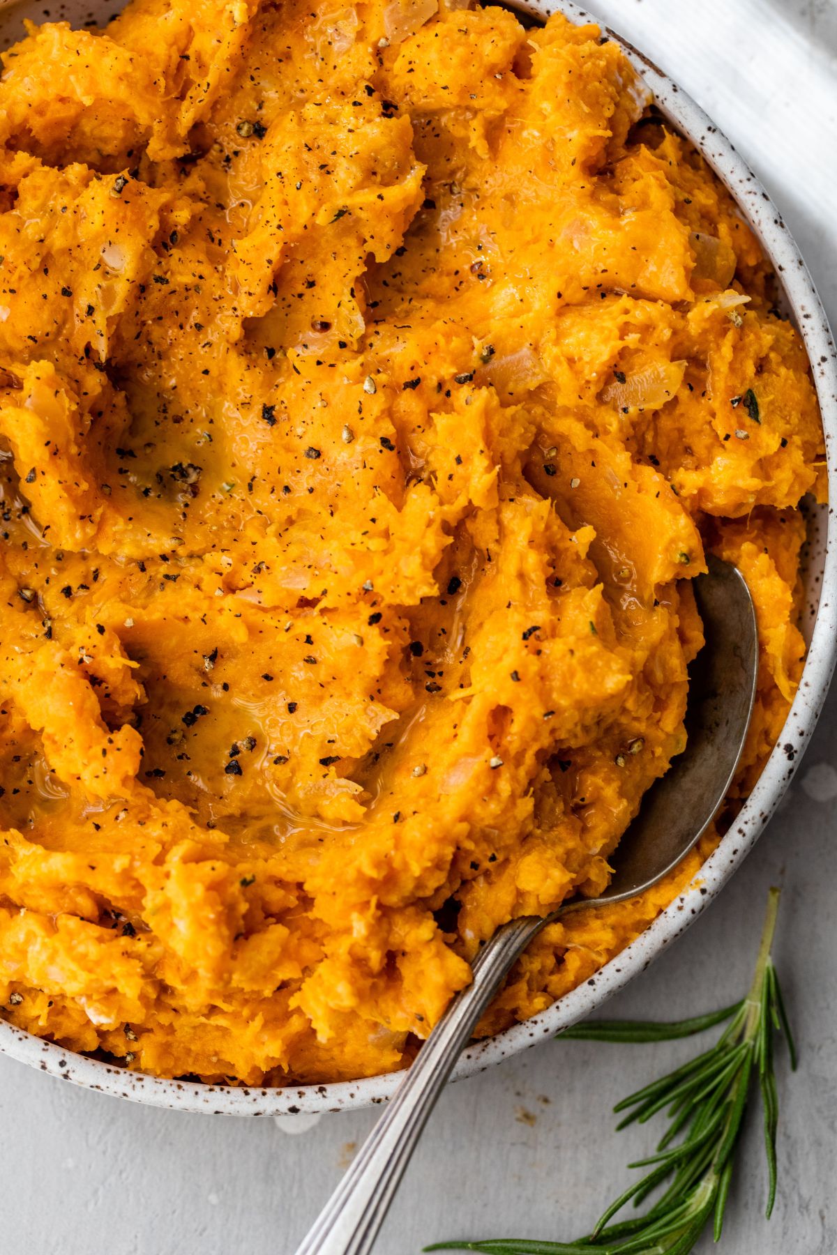 Healthy mashed sweet potatoes in a white bowl with a spoon.