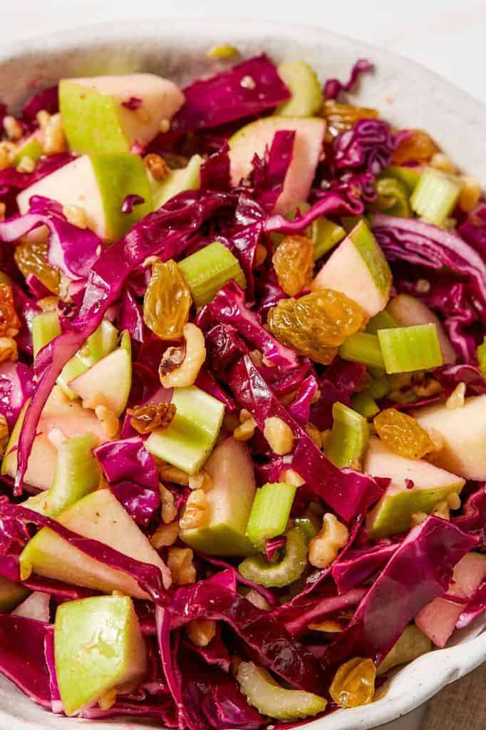 bowl filled with red cabbage, green apple, and golden raisins
