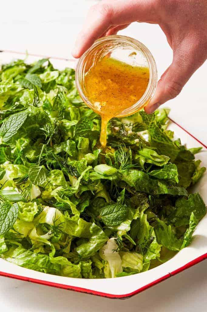 pouring lemon vinaigrette over a fresh green salad