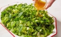 pouring lemon vinaigrette over romain lettuce salad