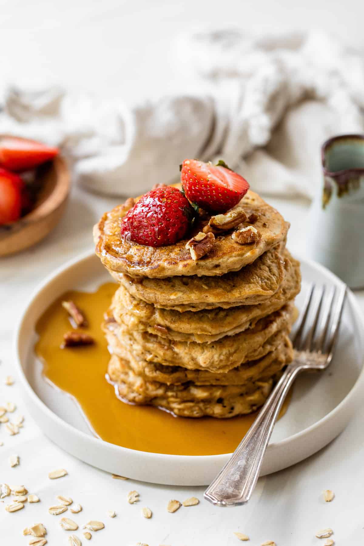 stack of oatmeal pancakes topped with strawberries and maple syrup
