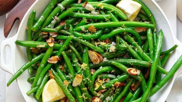 green bean almandine in a large white bowl near a small bowl of almonds
