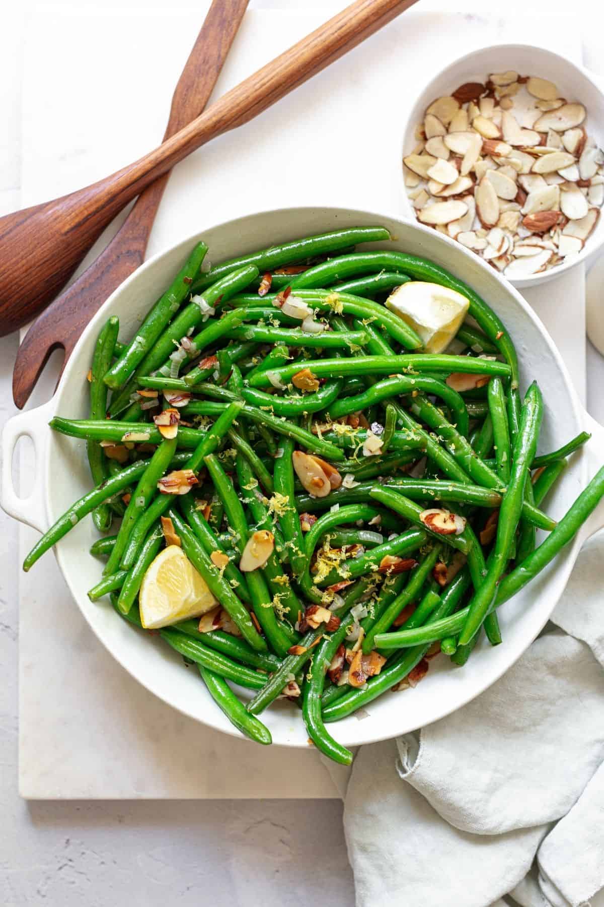 green bean almandine in a large white bowl near a small bowl of almonds