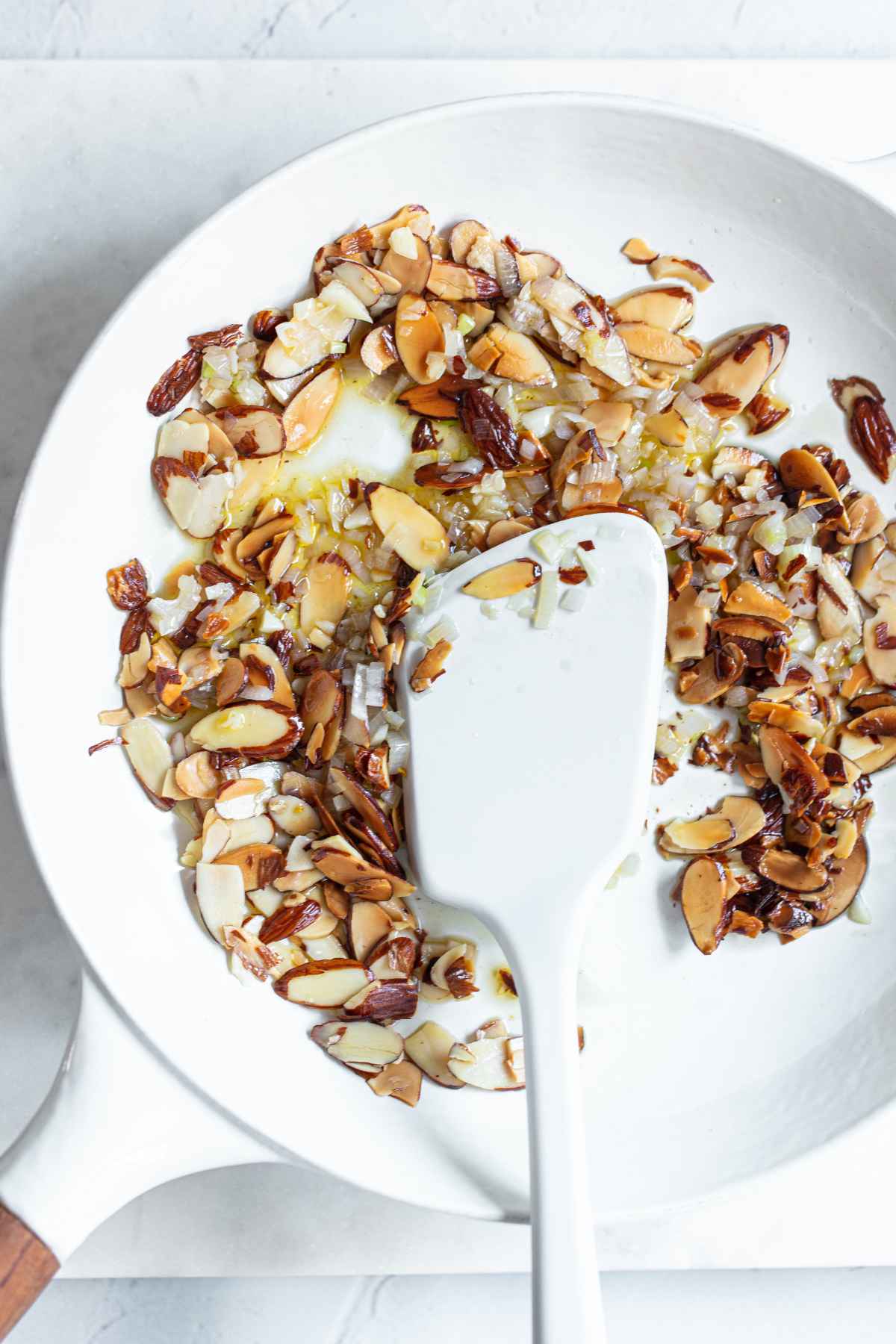 Toasting sliced almonds with a minced shallot and a minced garlic clove in a white skillet.