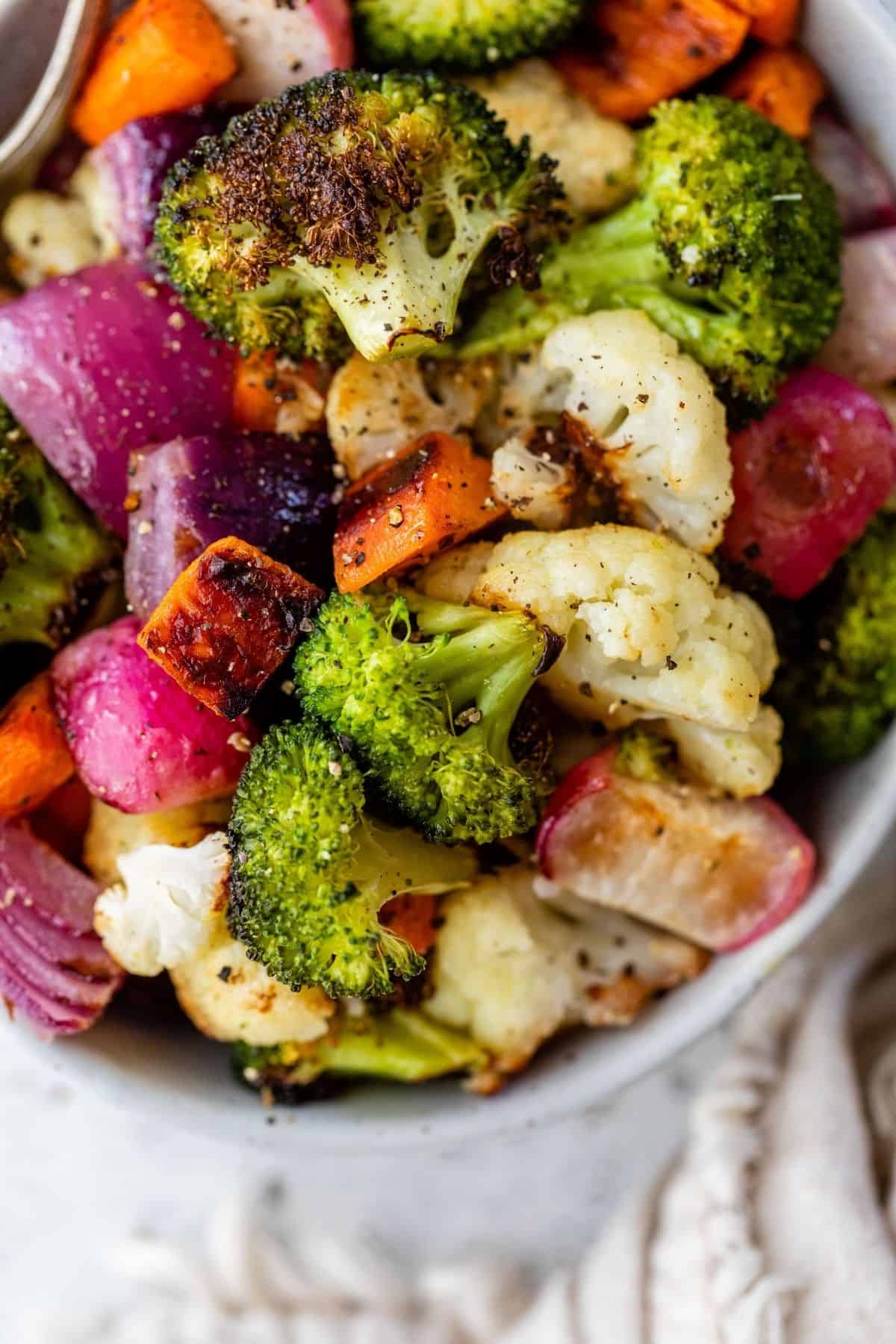 roasted broccoli, cauliflower, radishes and carrots in a white serving bowl