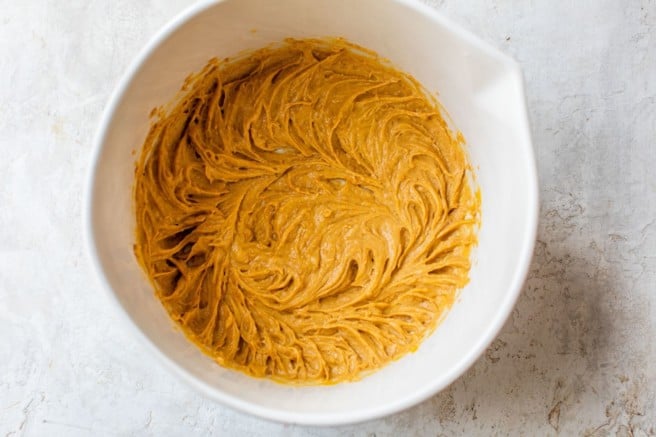 mixing peanut butter and pumpkin in a white mixing bowl