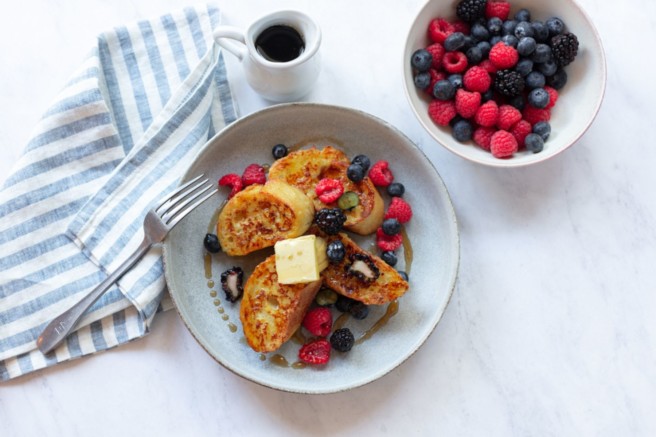 French toast served on a white plate with fruit and coffee.