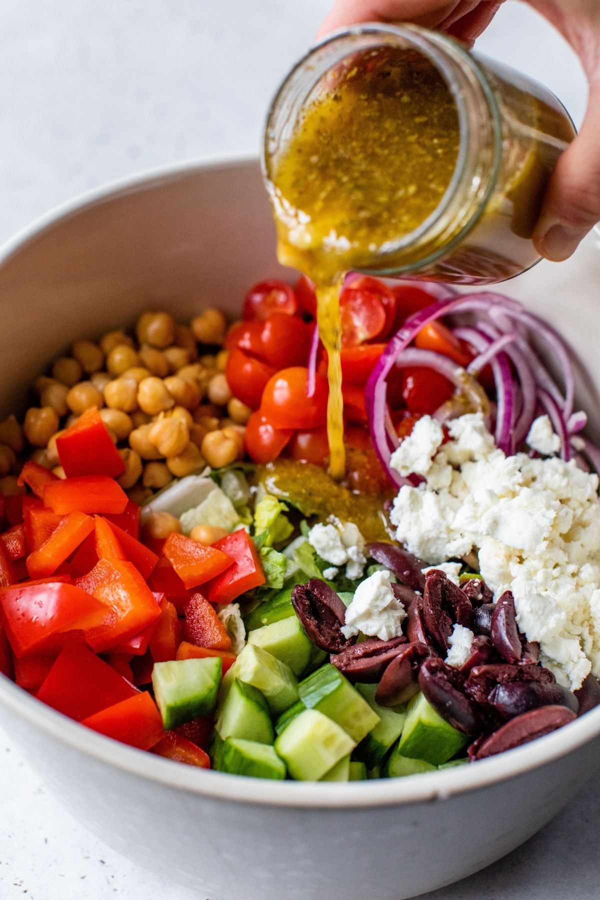 Pouring Greek salad dressing over a salad.