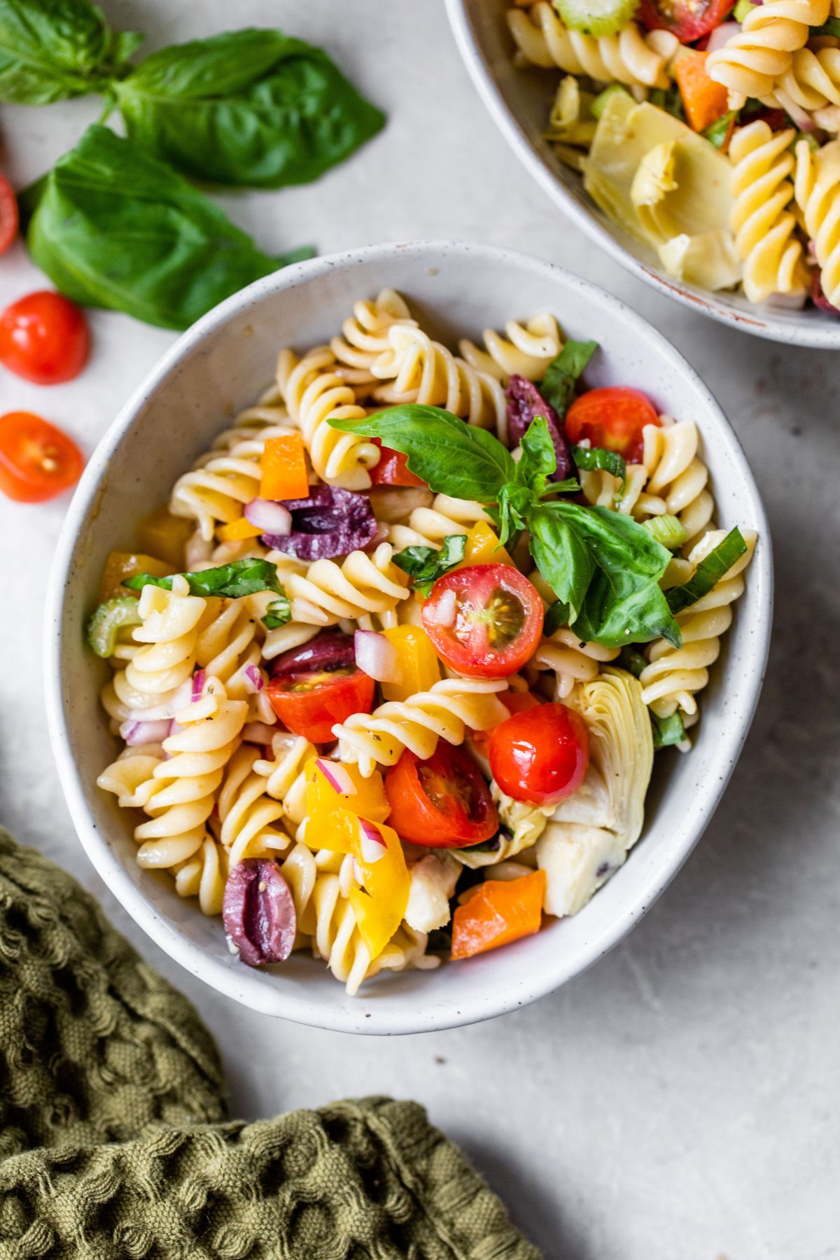 Pasta salad with tomatoes and fresh basil in a white bowl.
