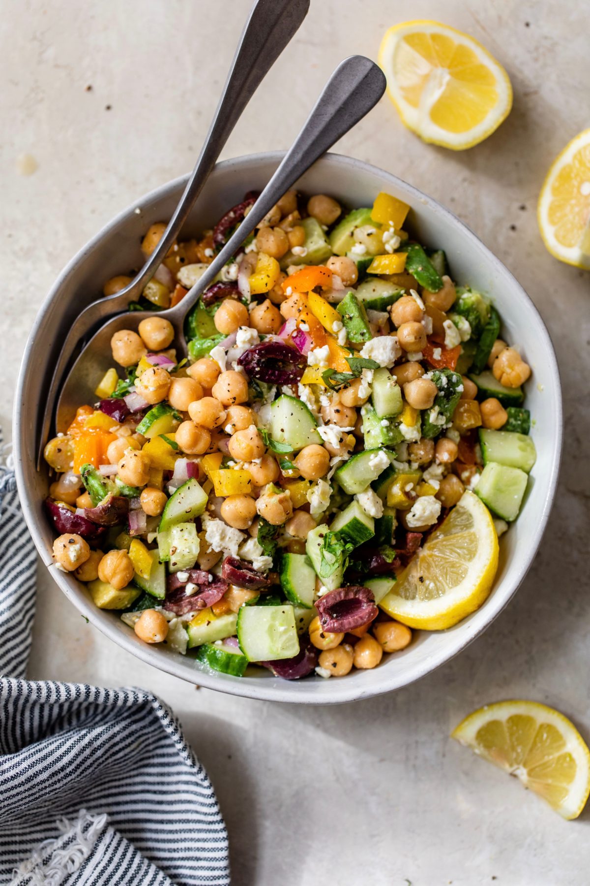mediterranean chickpea salad in white bowl with fork and spoon.