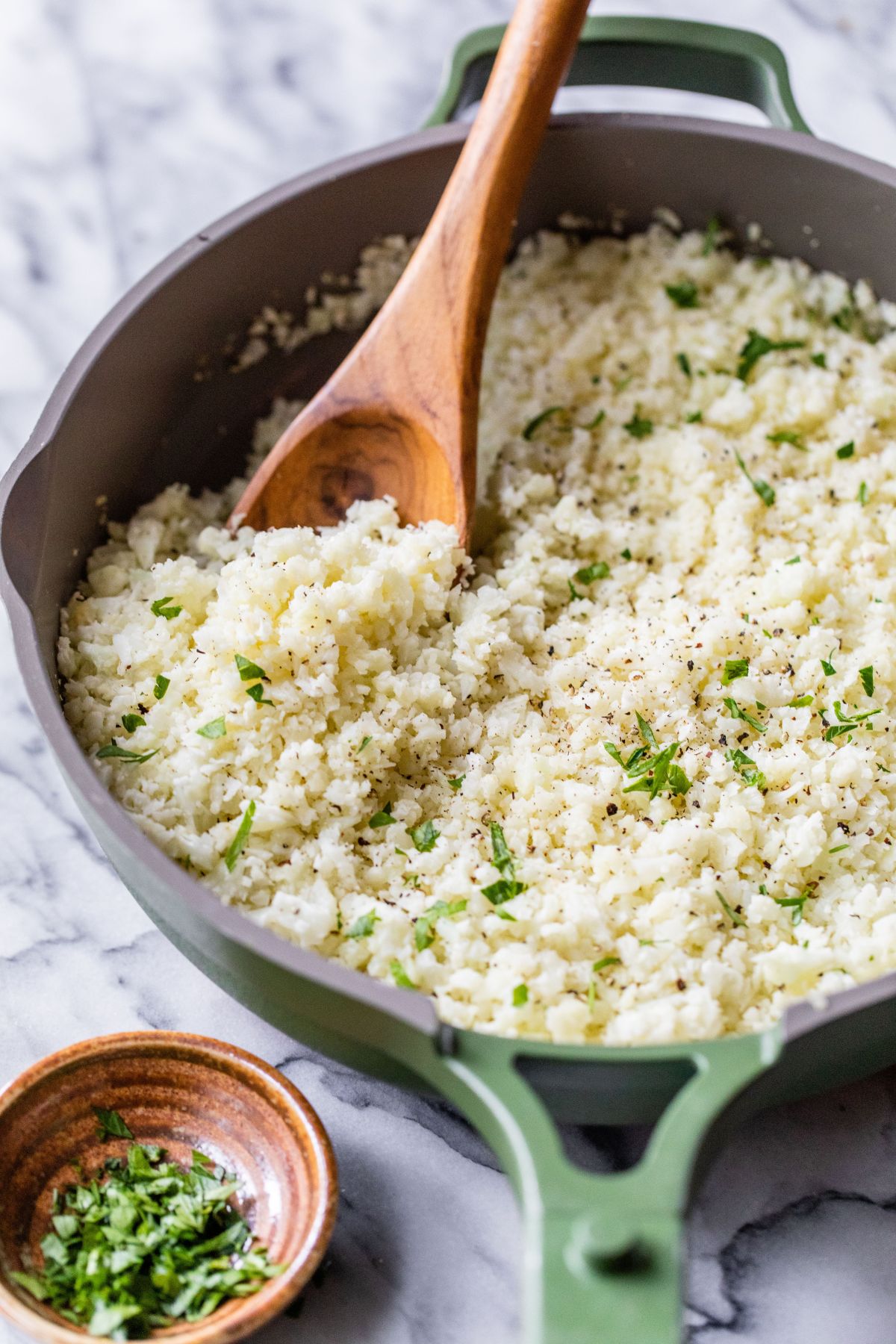 Cooking cauliflower rice in a skillet with a wooden spoon.
