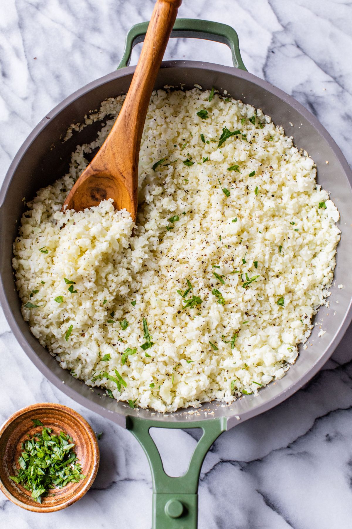 Cauliflower rice in a skillet with a wooden spoon.