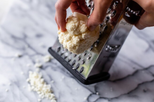 Grating a chunk of cauliflower on a box grater.