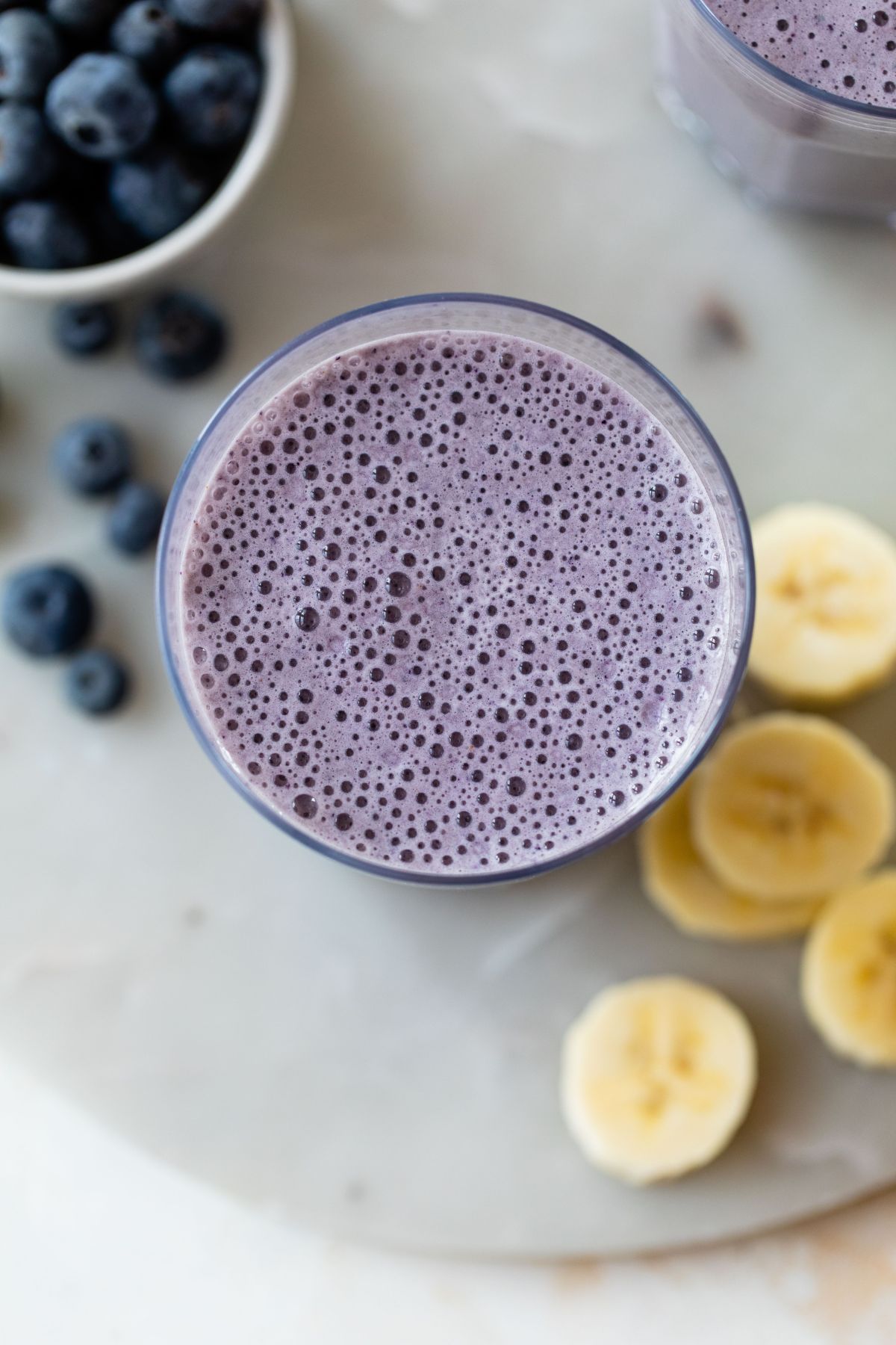 A blueberry smoothie near fresh blueberries and banana slices.