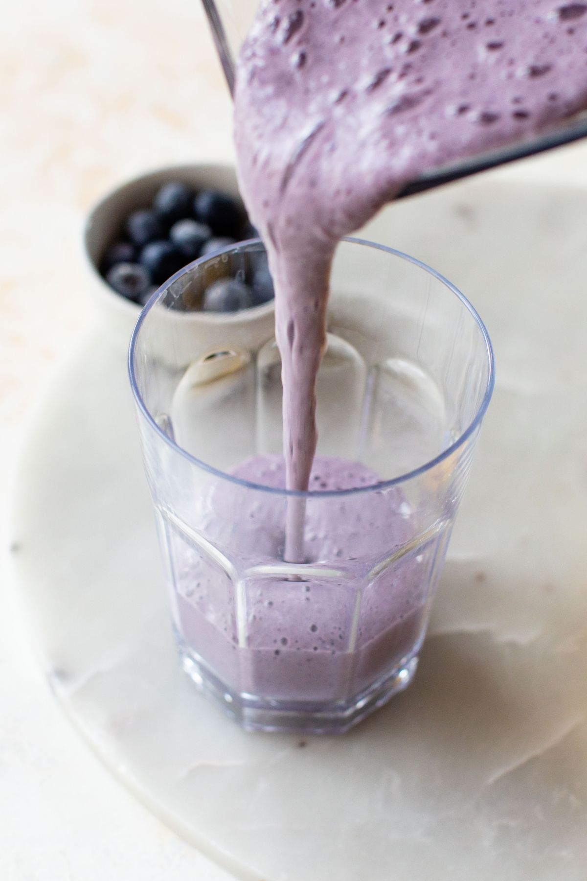 Pouring a blue smoothie into a glass from a blender.