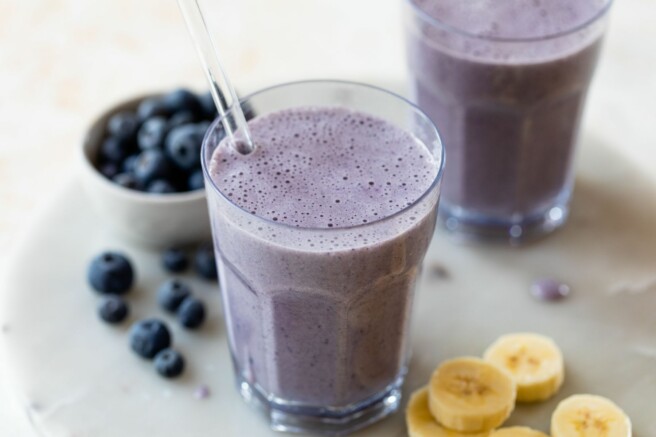 A blueberry banana smoothie near fresh blueberries and banana slices.
