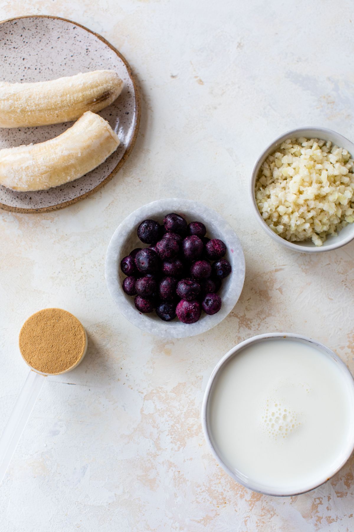 Blueberries, frozen banana, milk and cauliflower divided into small bowls.