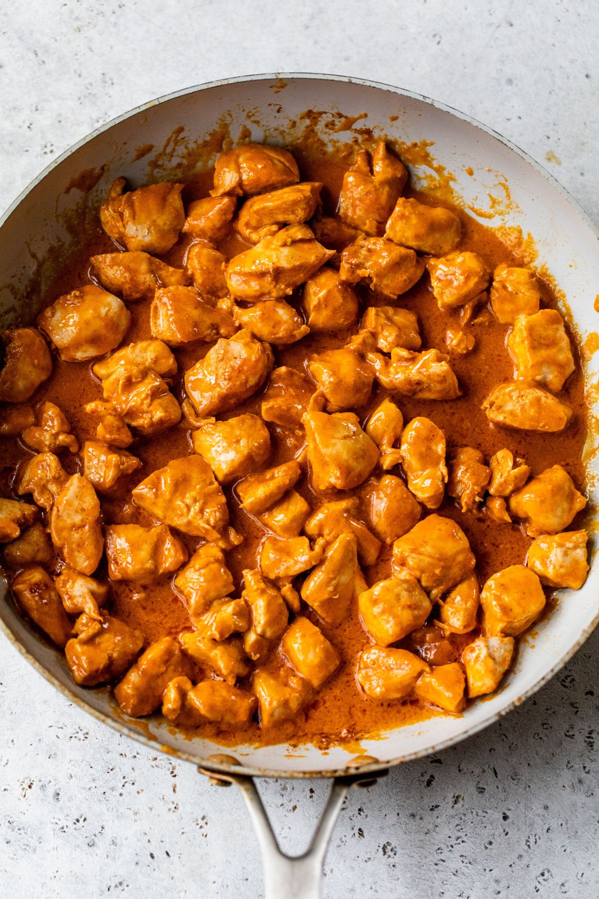 Stirring buffalo sauce with chicken bites in a skillet.