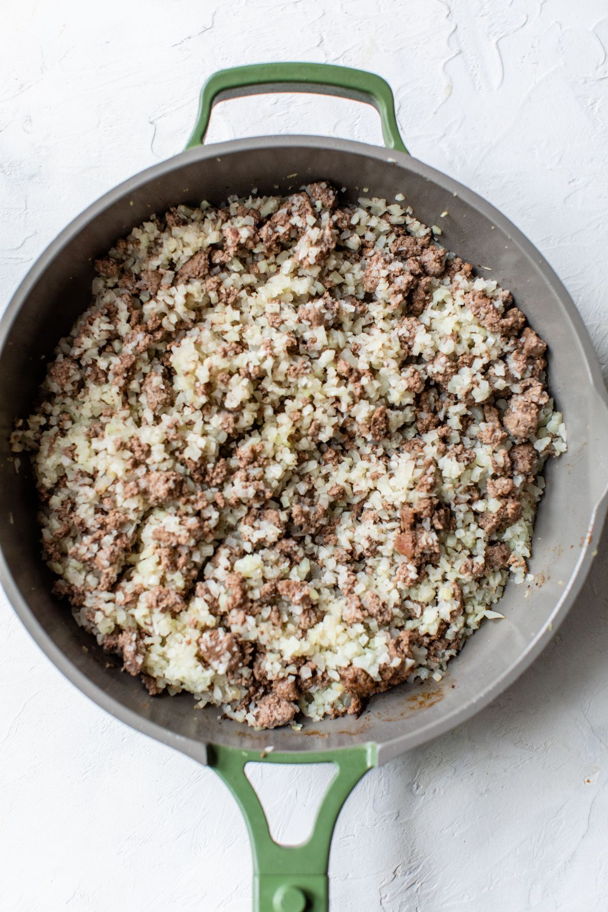 Cauliflower rice added to browned ground beef in a skillet.