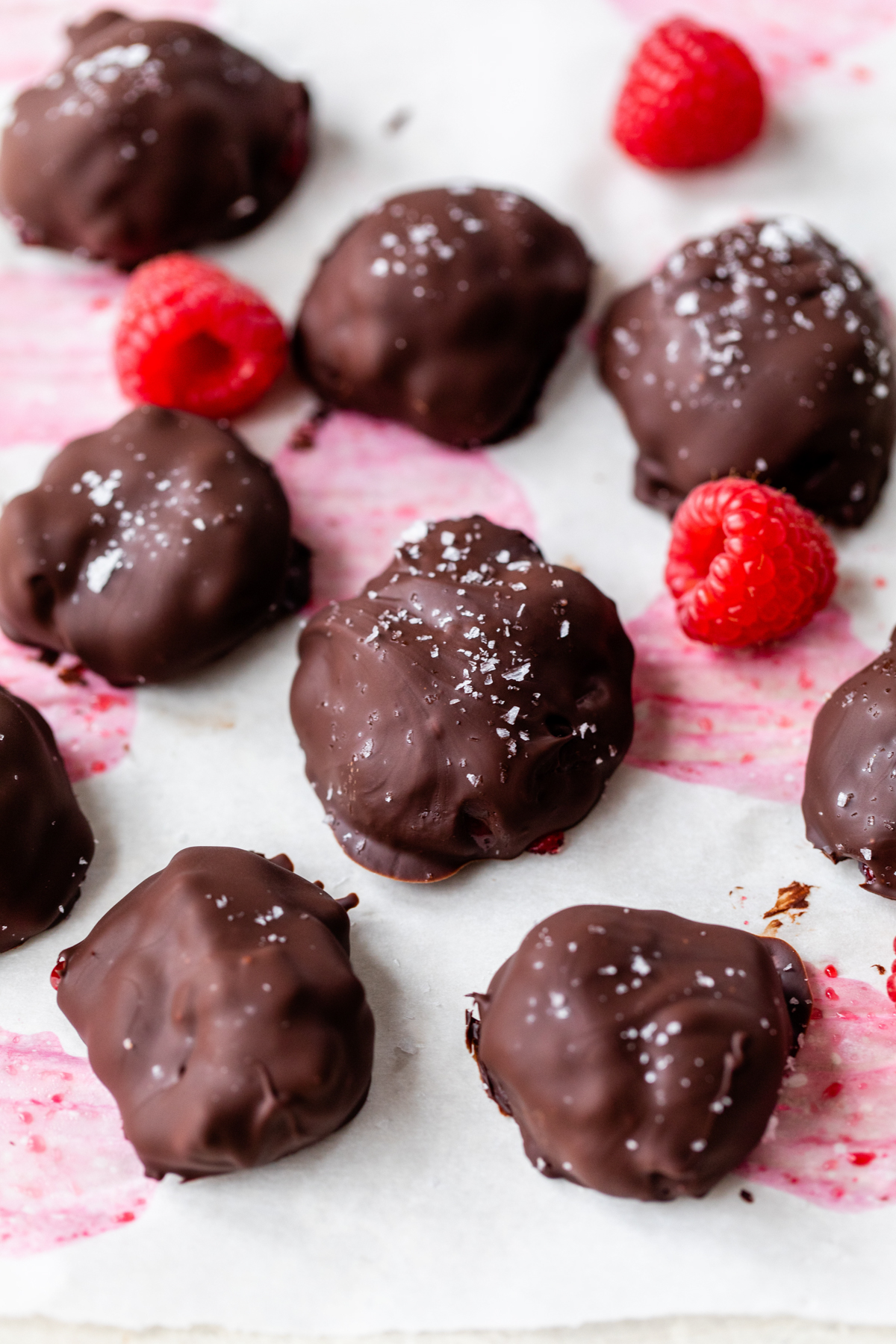 chocolate covered raspberry bites on white parchment paper surrounded by fresh strawberries