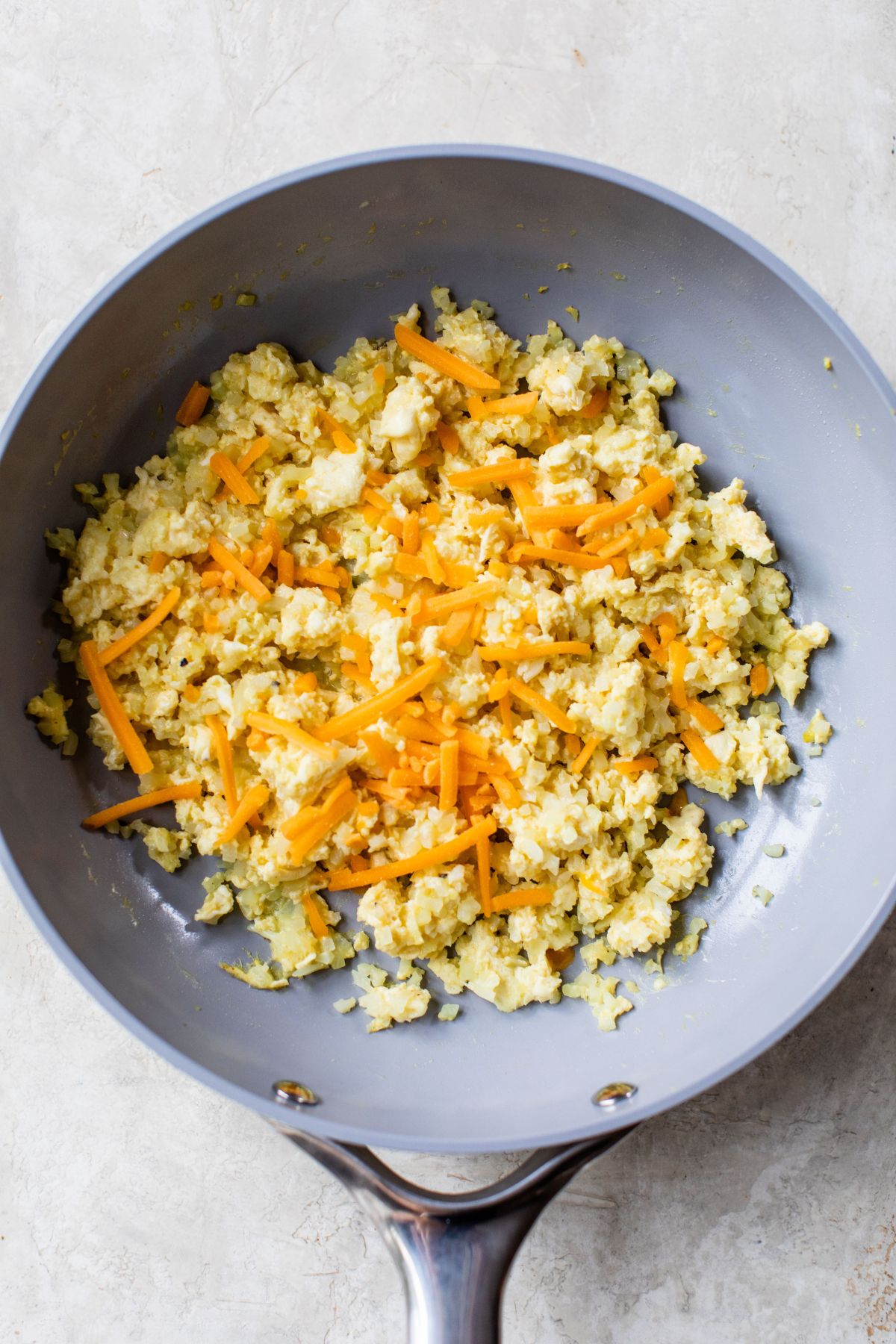 Grated cheese sprinkled over eggs in a pan.