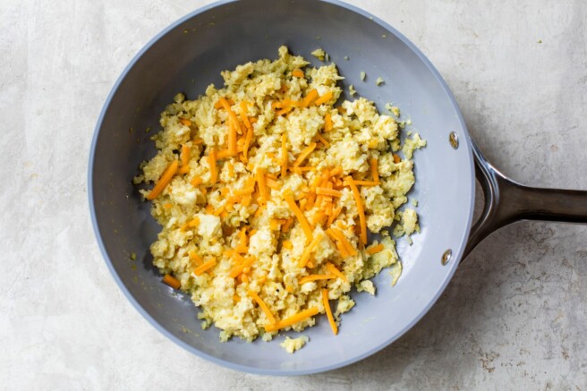Cheese sprinkled over scrambled eggs in a pan.