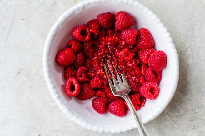 fresh raspberries in a white bowl with a fork for mashing