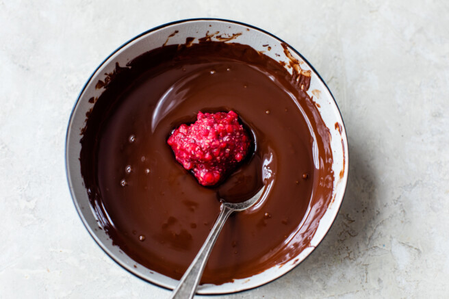 frozen raspberry rounds dipped in a bowl of melted chocolate