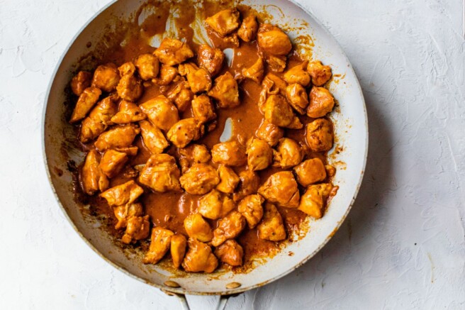 Adding buffalo sauce to chicken pieces a skillet.