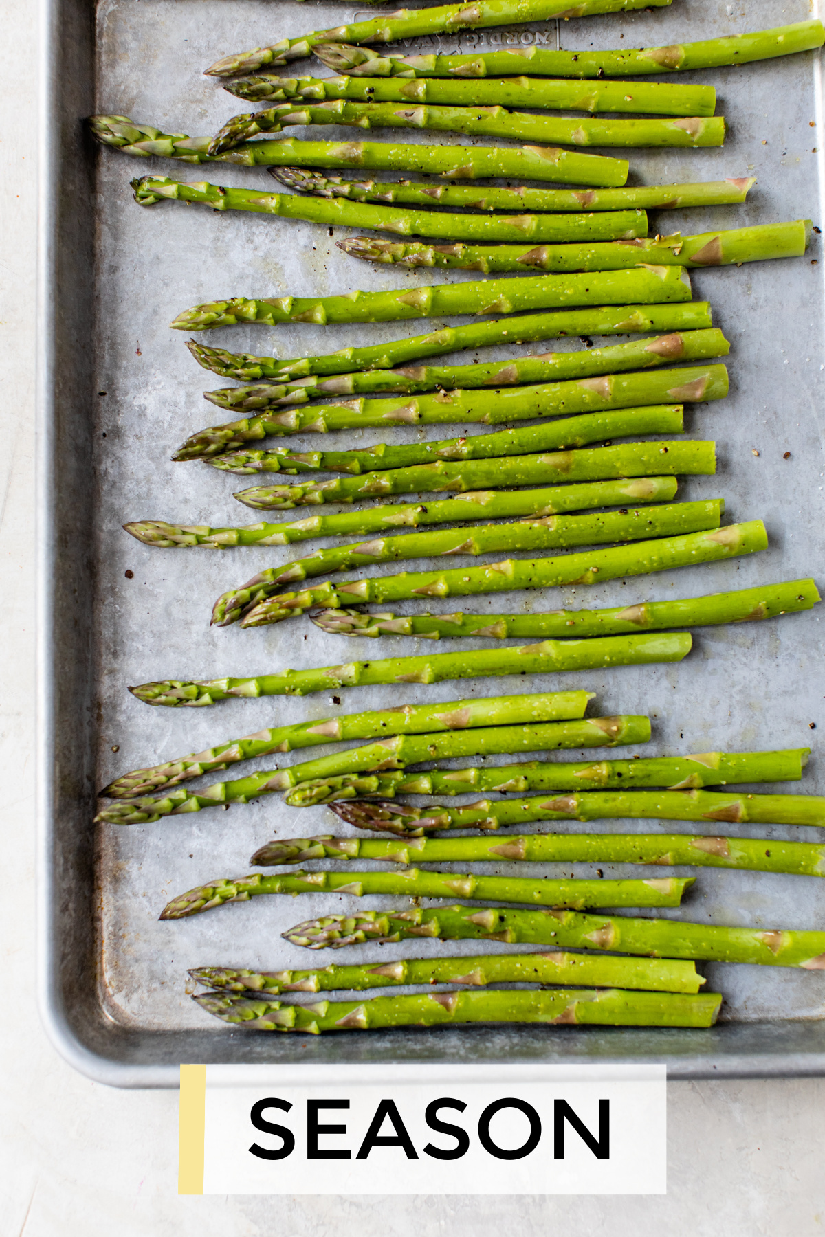 Asparagus on a rimmed baking tray seasoned with salt pepper and olive oil.