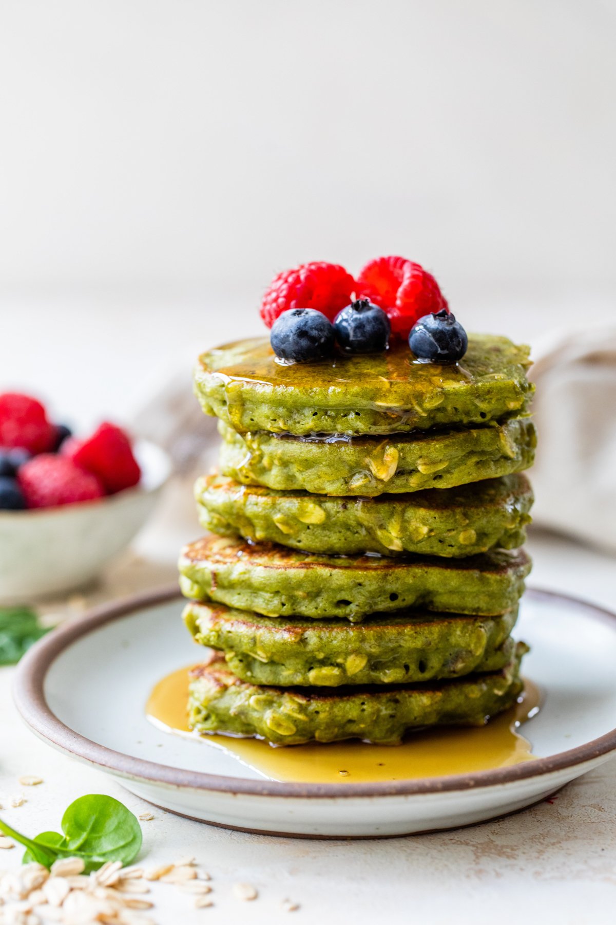 stack of spinach pancakes with oats on a plate topped with berries