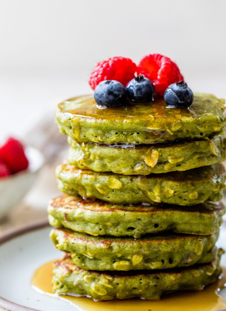 Stack of healthy spinach pancakes topped with oats and berries