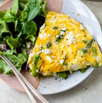 Slice of asparagus frittata on a white plate with a salad.
