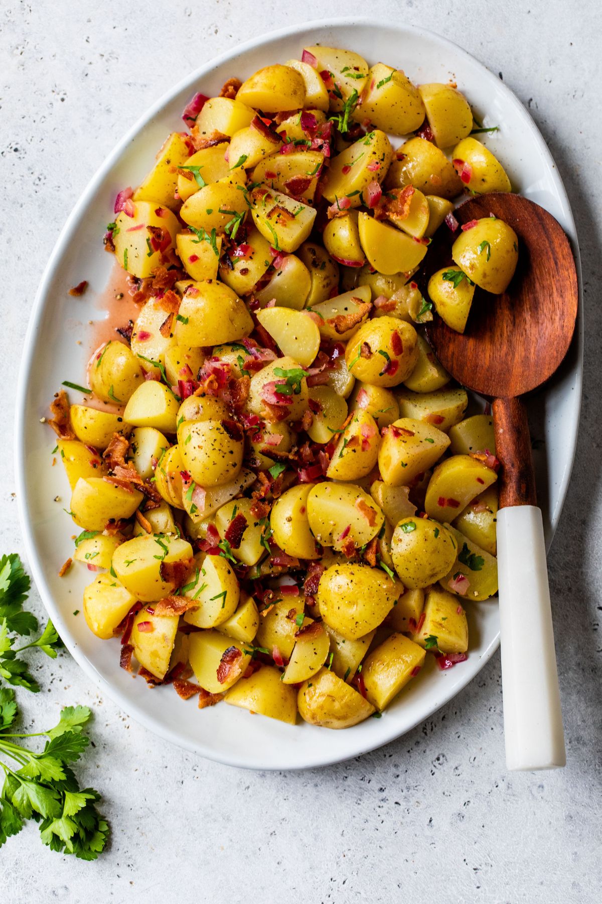 German Potato Salad topped with fresh parsley on a white platter.