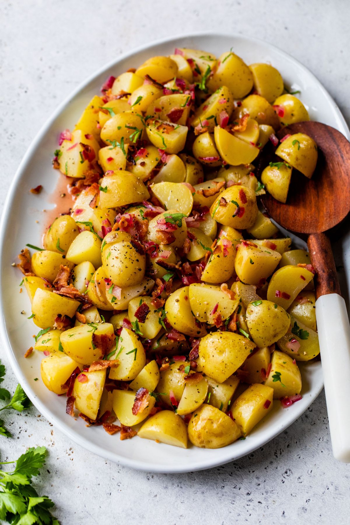 German potato salad served on a large white platter with a wooden serving spoon.