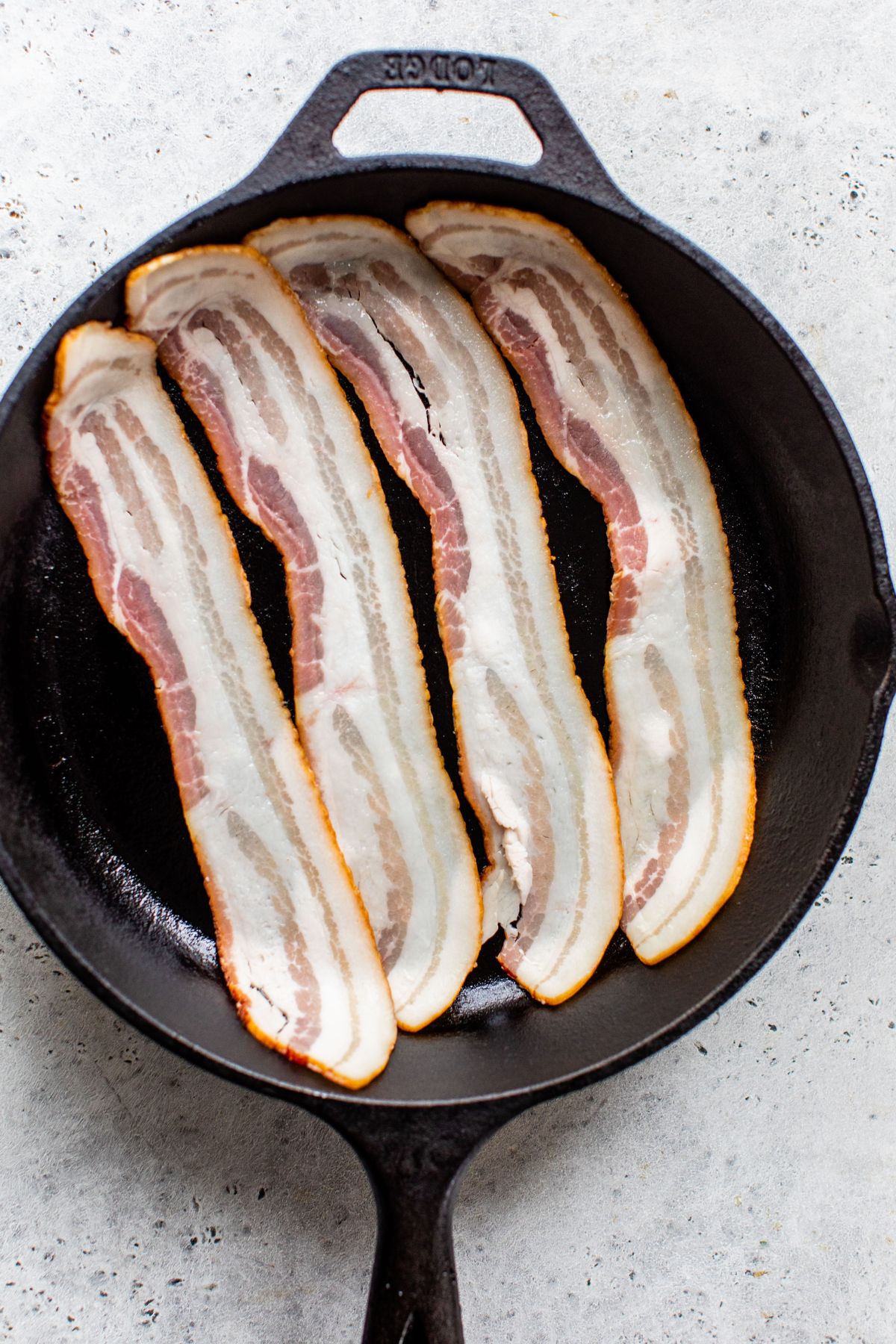 Four slices of bacon in a cast iron skillet.
