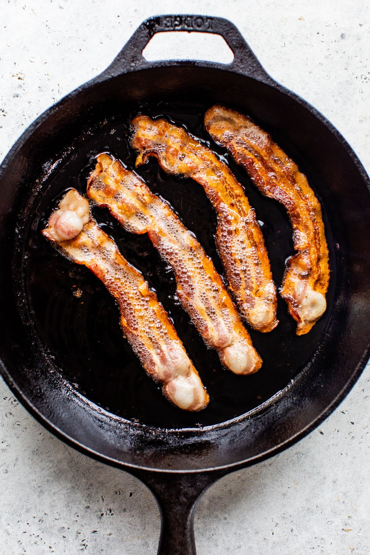 Cooking slices of bacon in a large skillet.