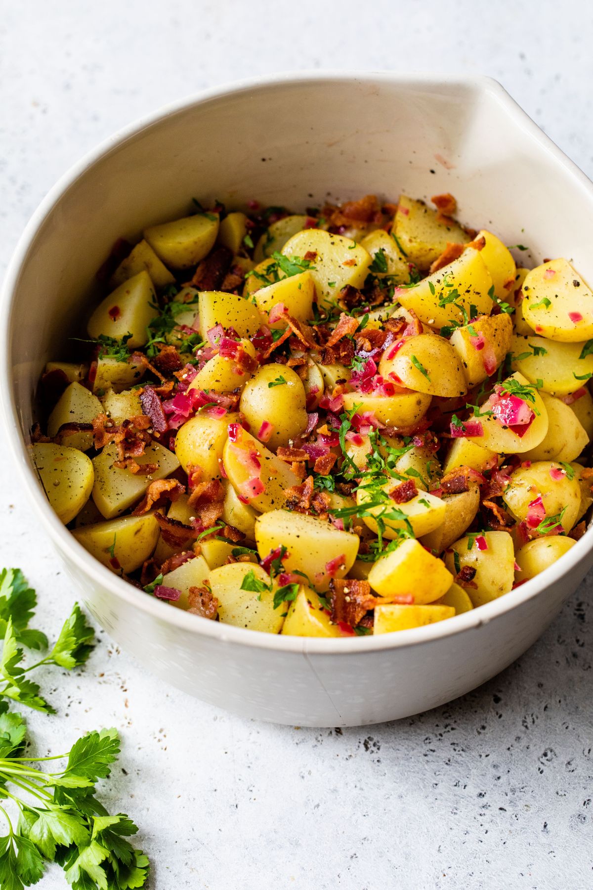 White bowl filled with cooked red potatoes, bacon pieces and fresh parsley.